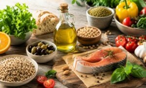 Ingredienti tipici della dieta mediterranea con olio extravergine d’oliva, pesce, legumi, cereali integrali e verdure fresche disposti su un tavolo in legno.