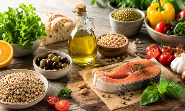 Ingredienti tipici della dieta mediterranea con olio extravergine d’oliva, pesce, legumi, cereali integrali e verdure fresche disposti su un tavolo in legno.